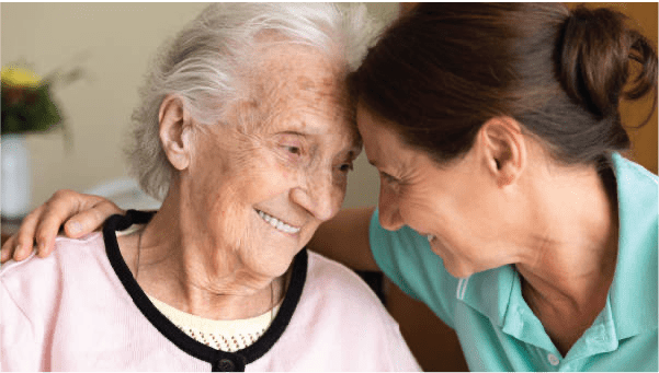 An elderly woman with dementia smiles at her caregiver