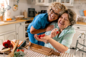 Caregiver and senior woman preparing salad together at home and having fan